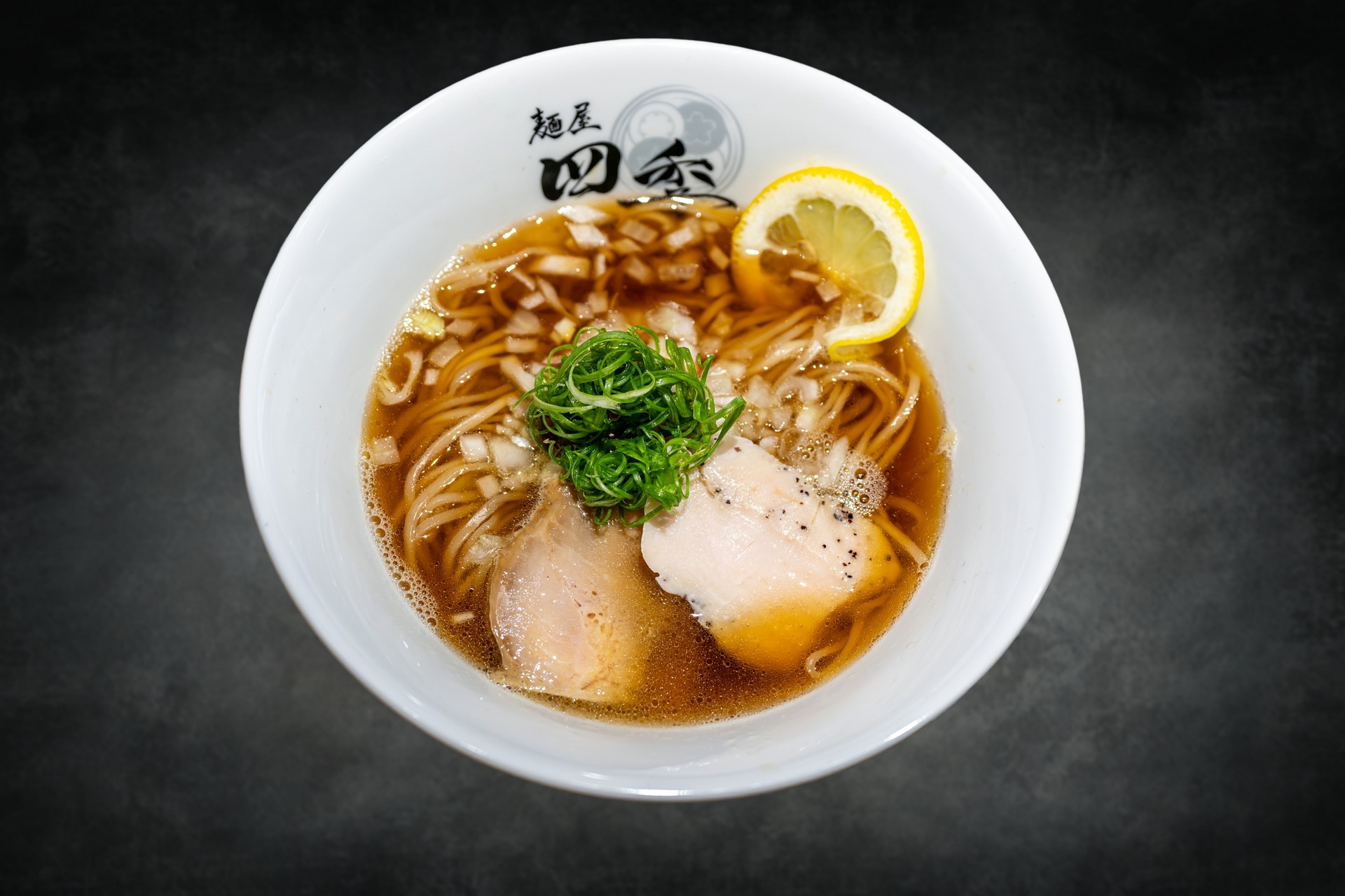 淡麗雞清湯拉麵，琥珀色雞湯搭配麵條、叉燒、蔥花與檸檬片